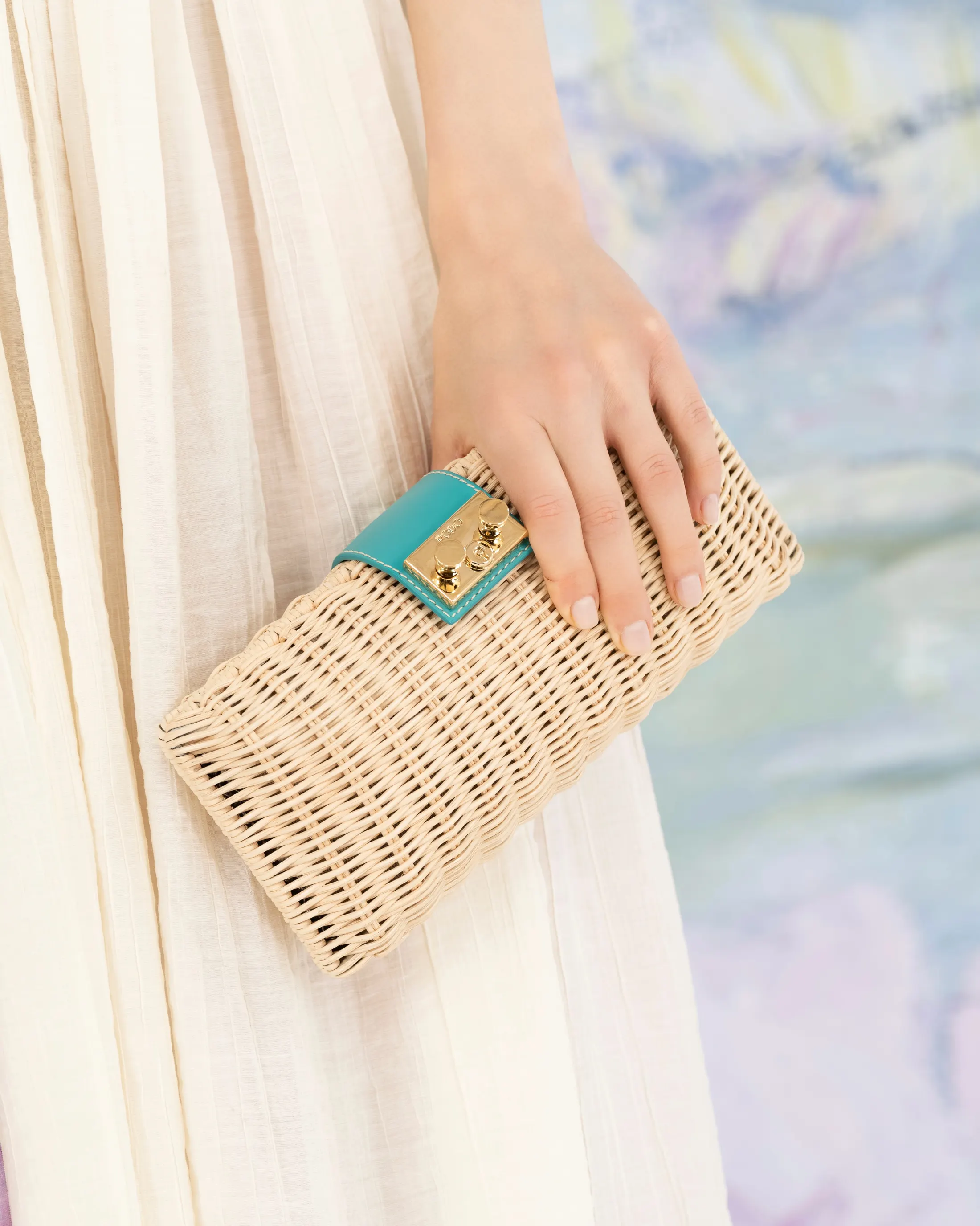 Pochette in paglia intrecciata tenuta davanti a un fondale che riproduce le ninfee di Monet