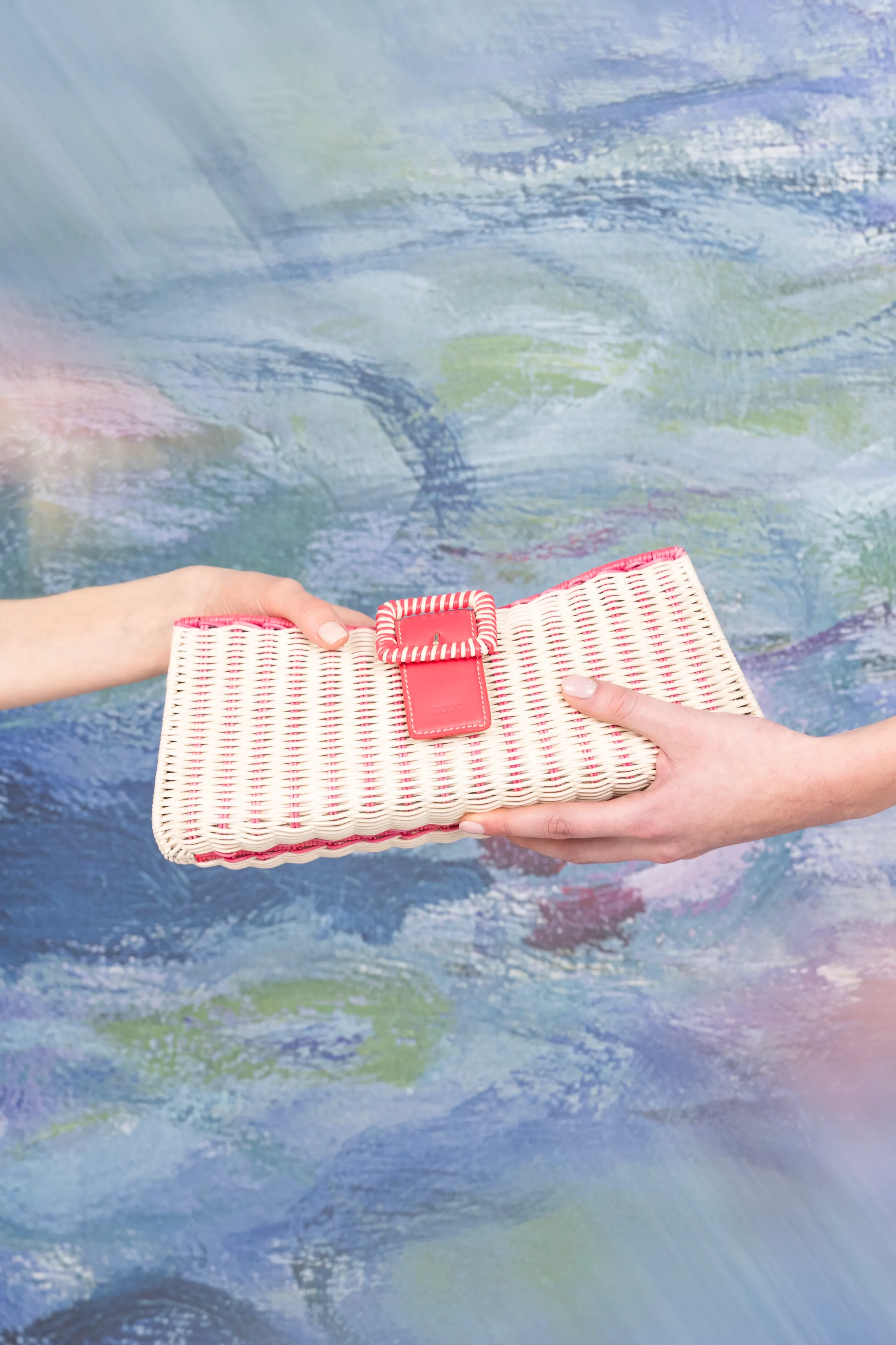Due mani che porgono una pochette intrecciata bianca e rossa davanti alle ninfee