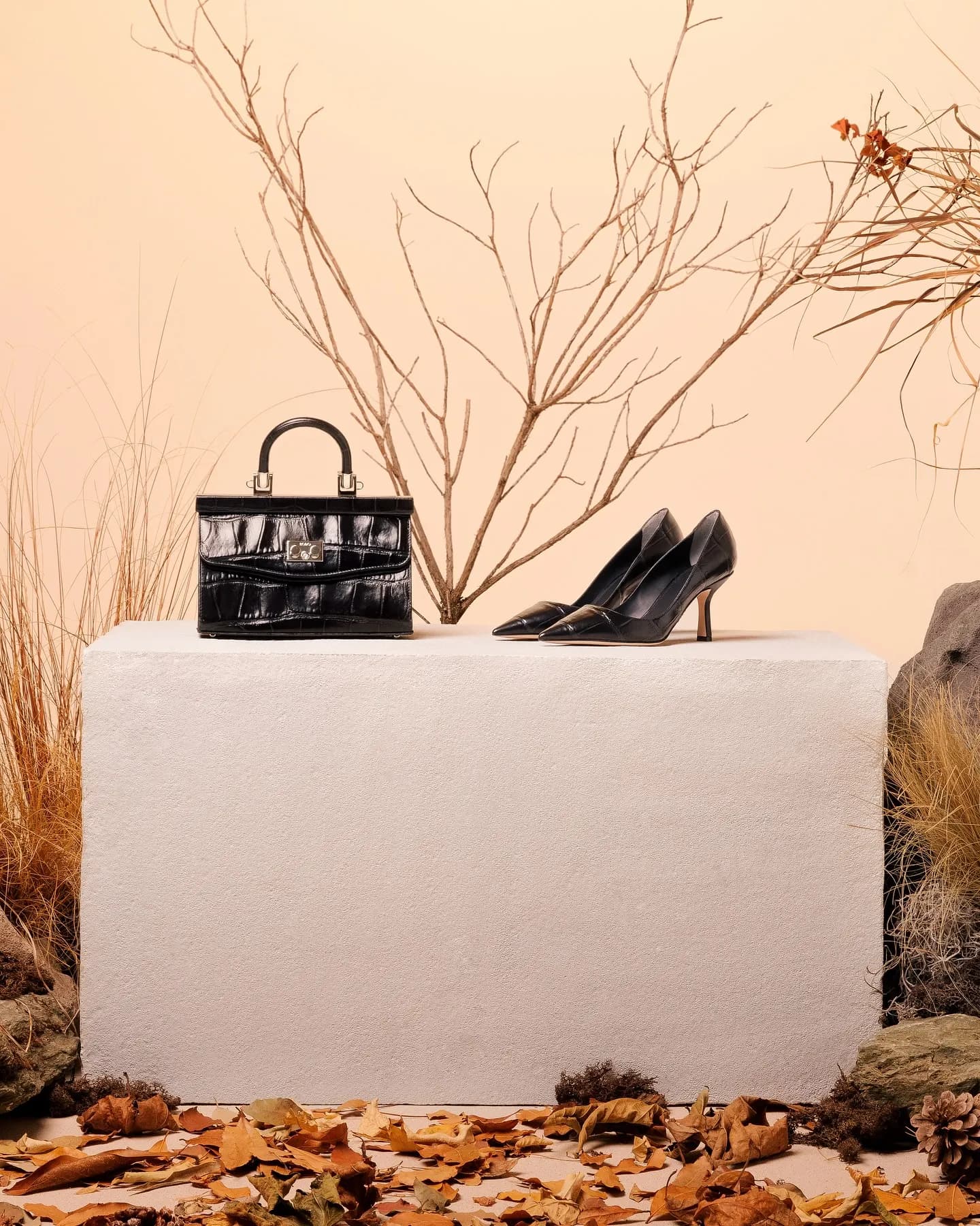 Gambe sedute su un blocco chiaro con clutch rossa arricciata, fra erbe secche e sassi