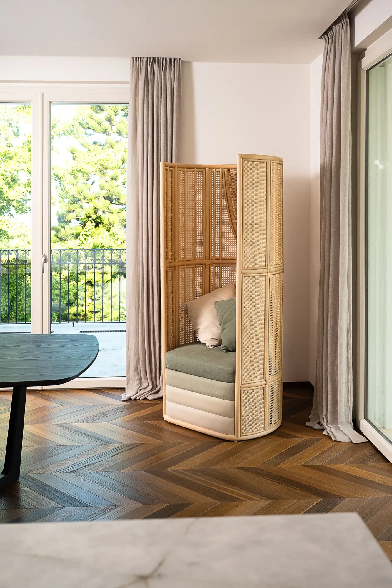 Poltrona paravento intrecciata in una stanza con parquet a spina ungherese e finestra sul giardino
