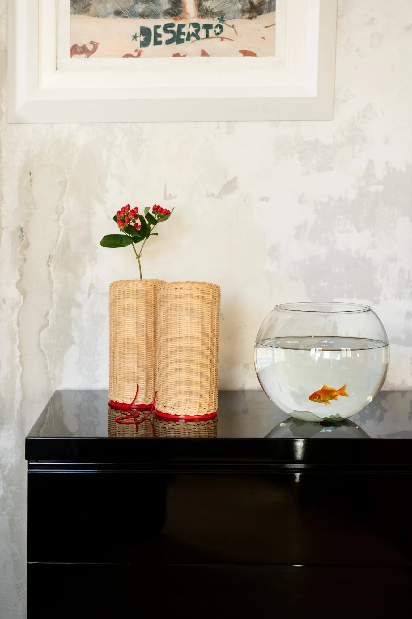 Due lampade in midollino e una boccia con un pesce rosso su una credenza nera lucida