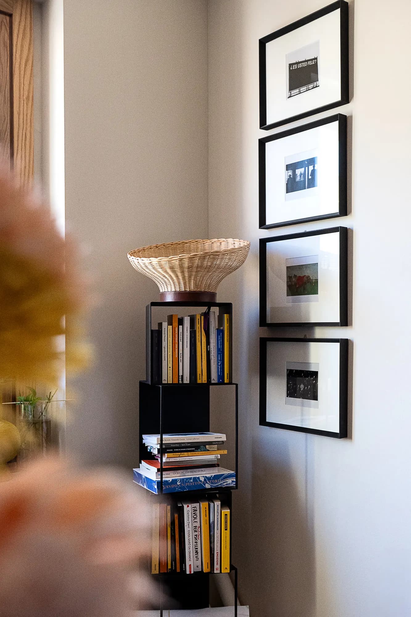 Lampada a cesto intrecciato su una libreria, accanto a stampe incorniciate