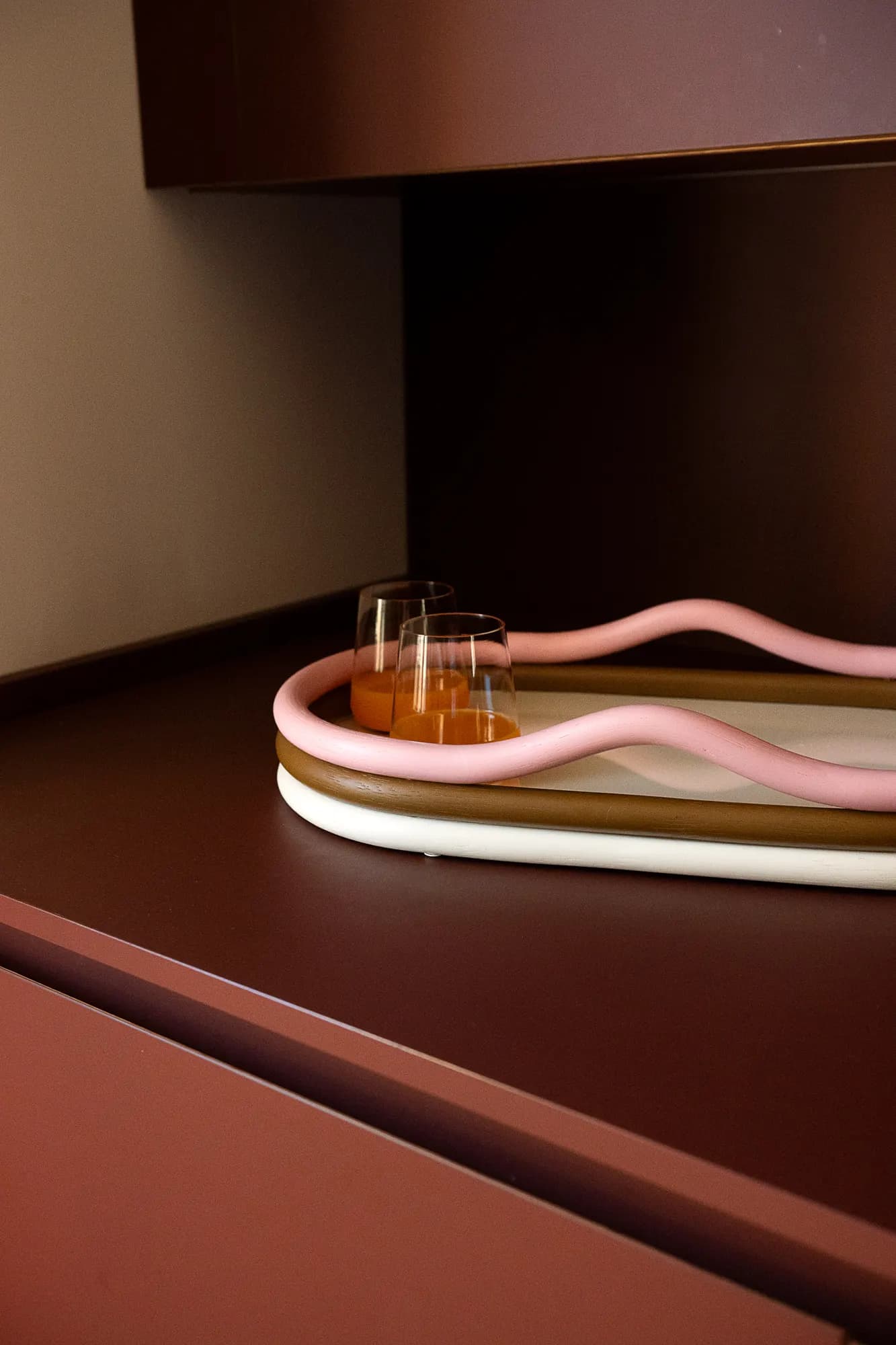 Vassoio curvo rosa con bicchieri su un piano bordeaux