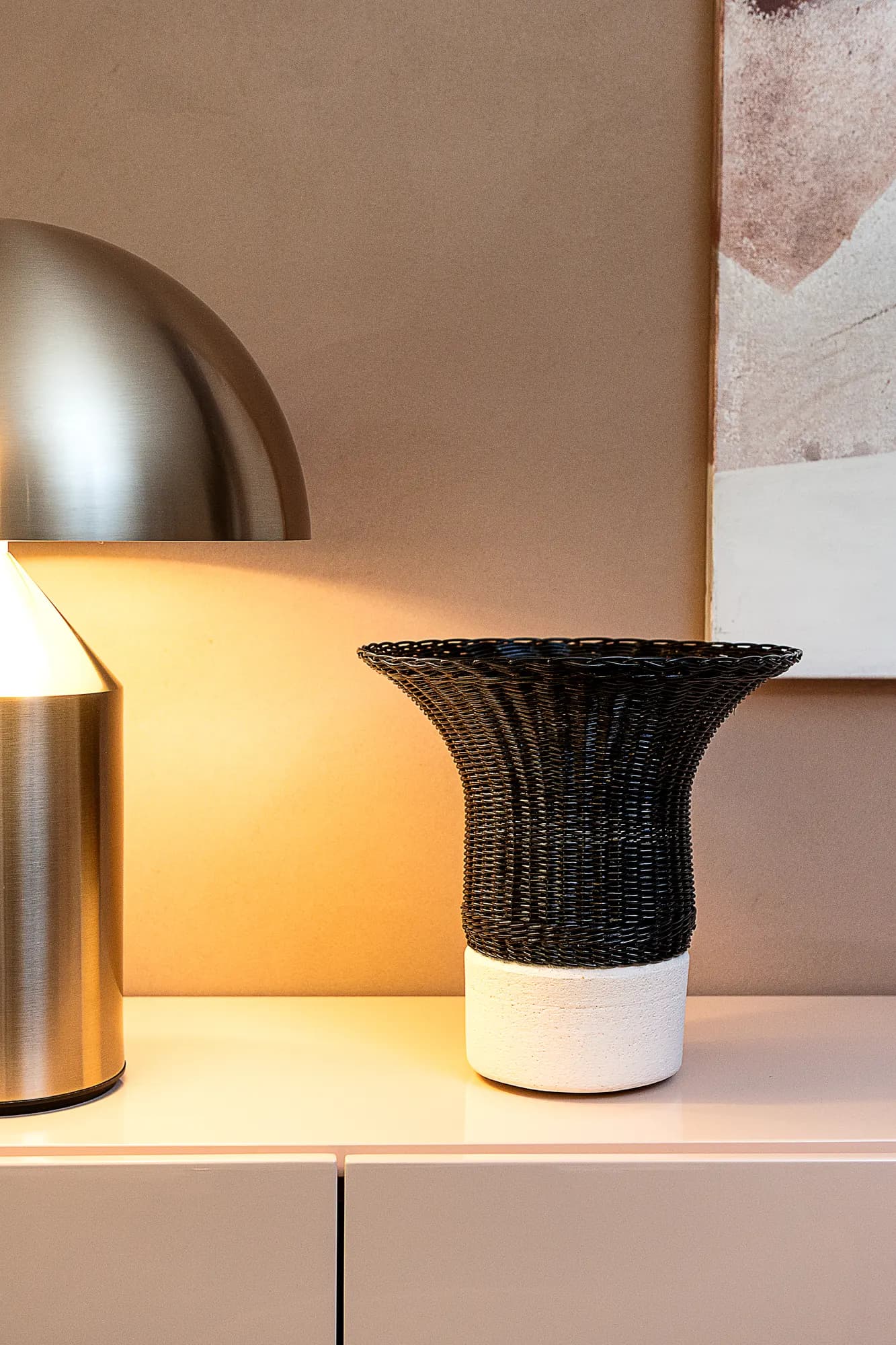 Vaso nero intrecciato sotto una lampada a cupola in ottone