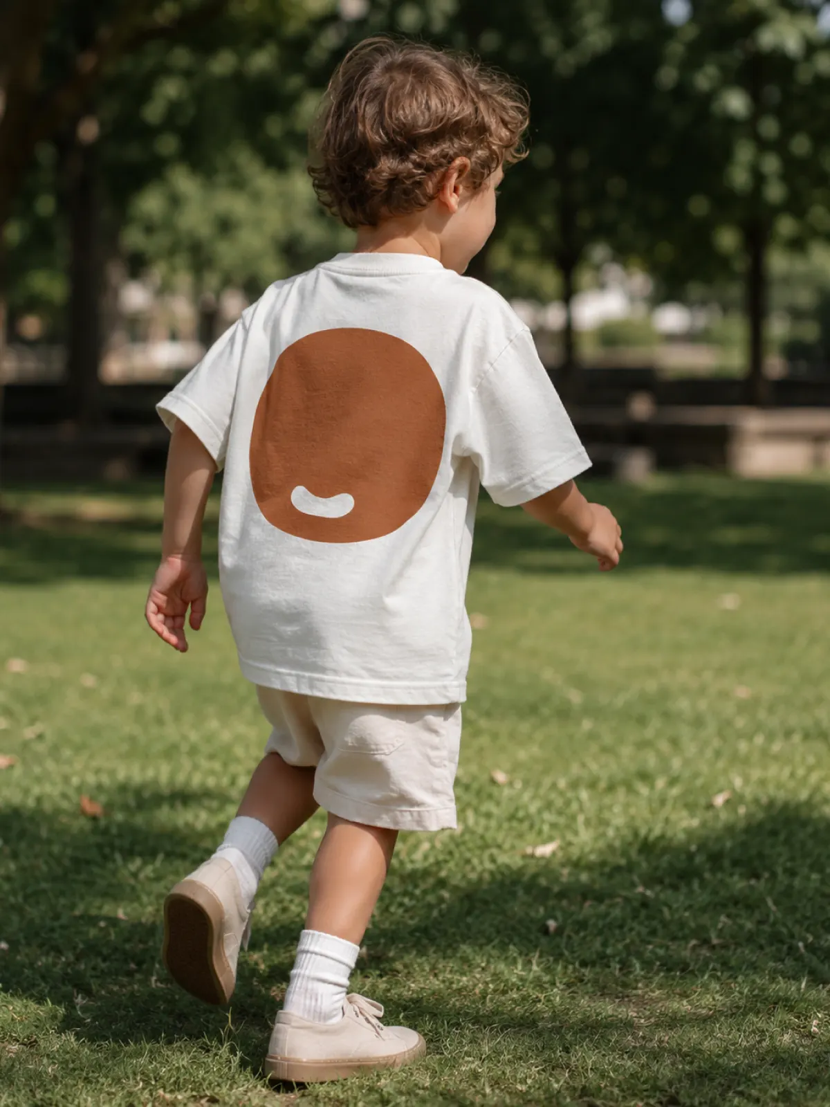 Bambino di spalle che corre su un prato, maglietta con la O del marchio