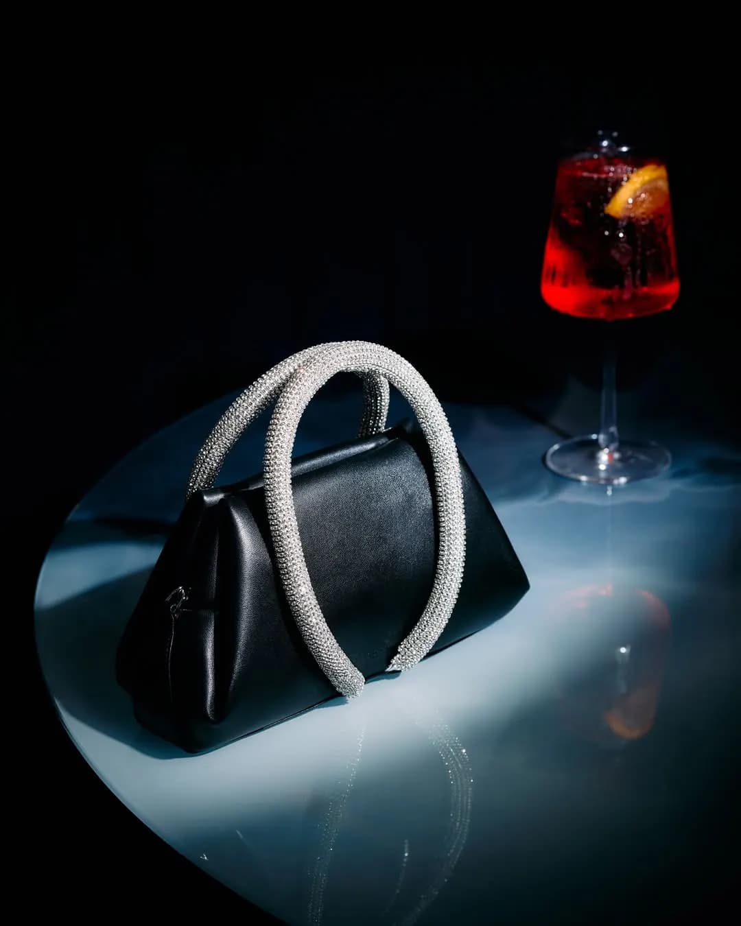 Borsa nera con manico di cristalli accanto a un calice, still life notturno