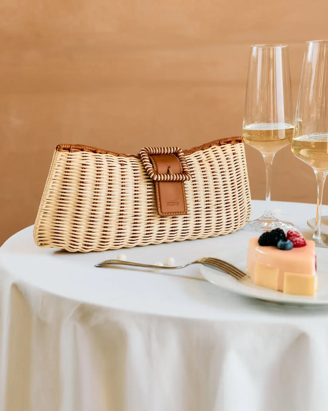 Pochette in vimini su una tavola apparecchiata, calici di spumante e dolce