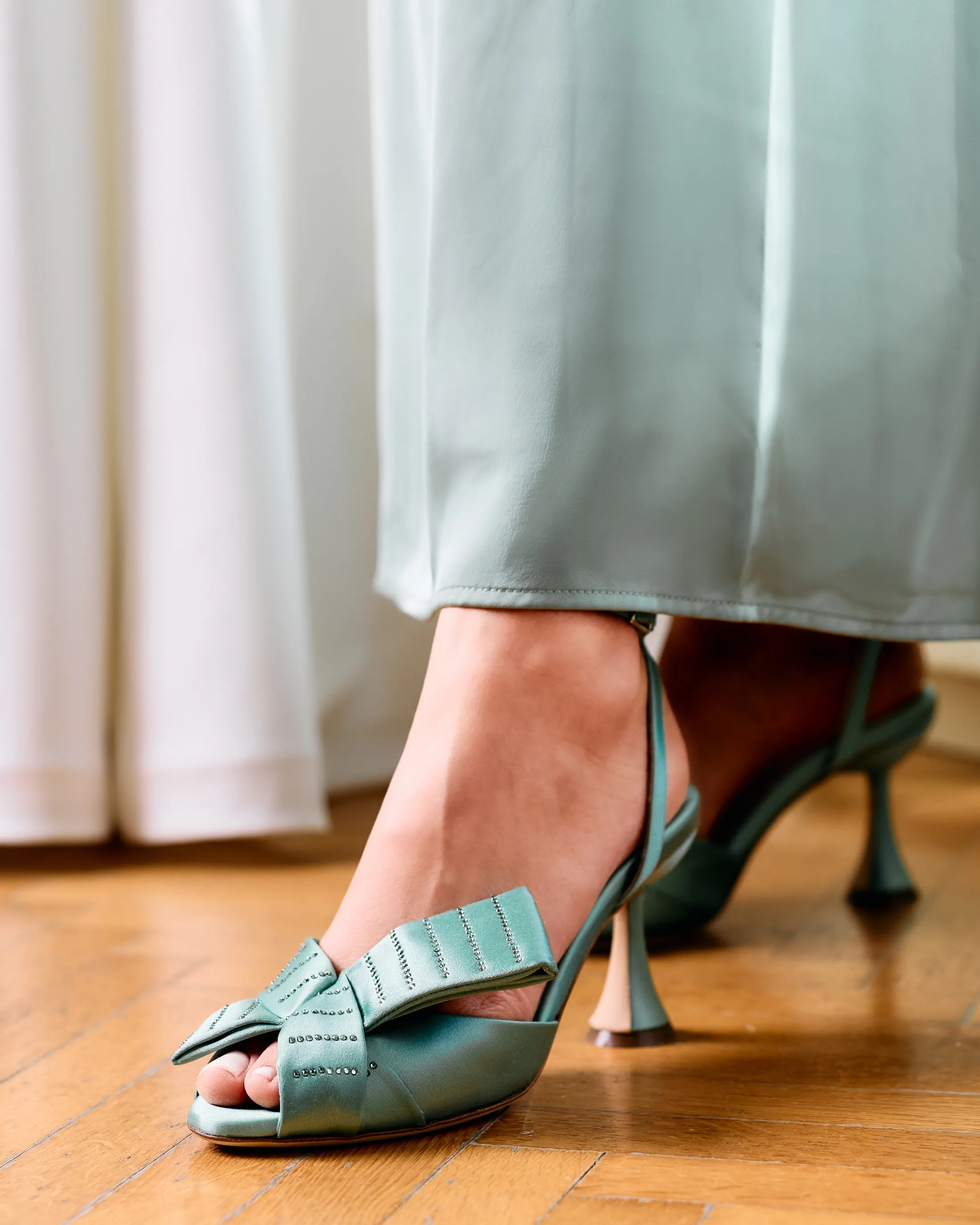 Slingback verde salvia con fiocco su un parquet, abito lungo in raso
