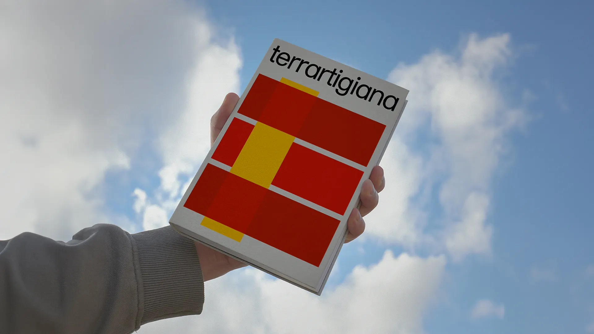 Mano che regge la copertina del catalogo contro il cielo