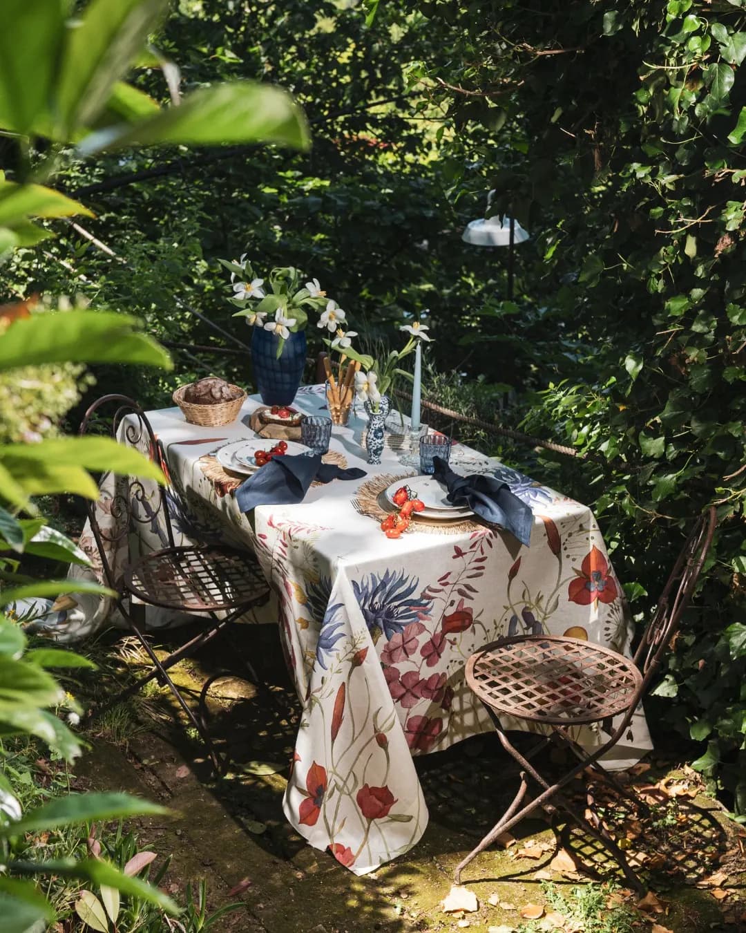 Tavola apparecchiata in giardino sotto le fronde, tovaglia in lino a stampa botanica