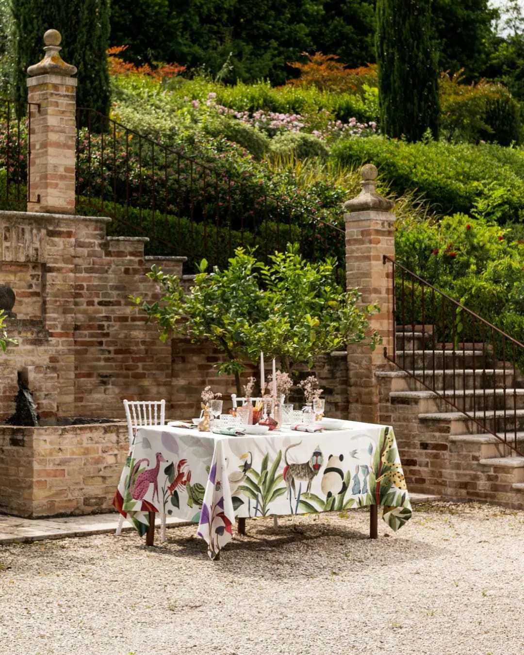 Tavola su una terrazza in mattoni fra i cipressi, tovaglia a stampa vegetale
