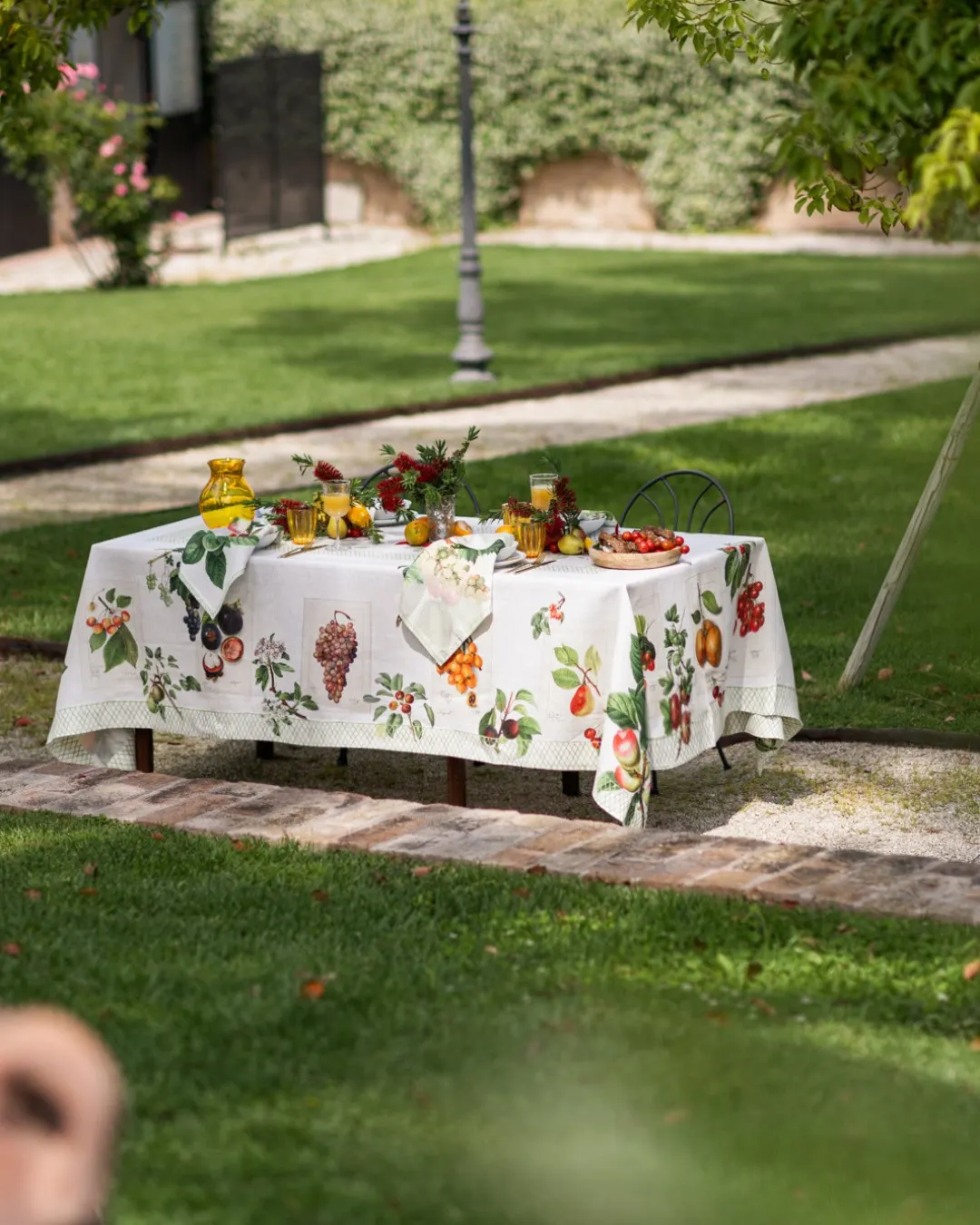 Tavola apparecchiata in giardino sotto le fronde, tovaglia in lino a stampa botanica