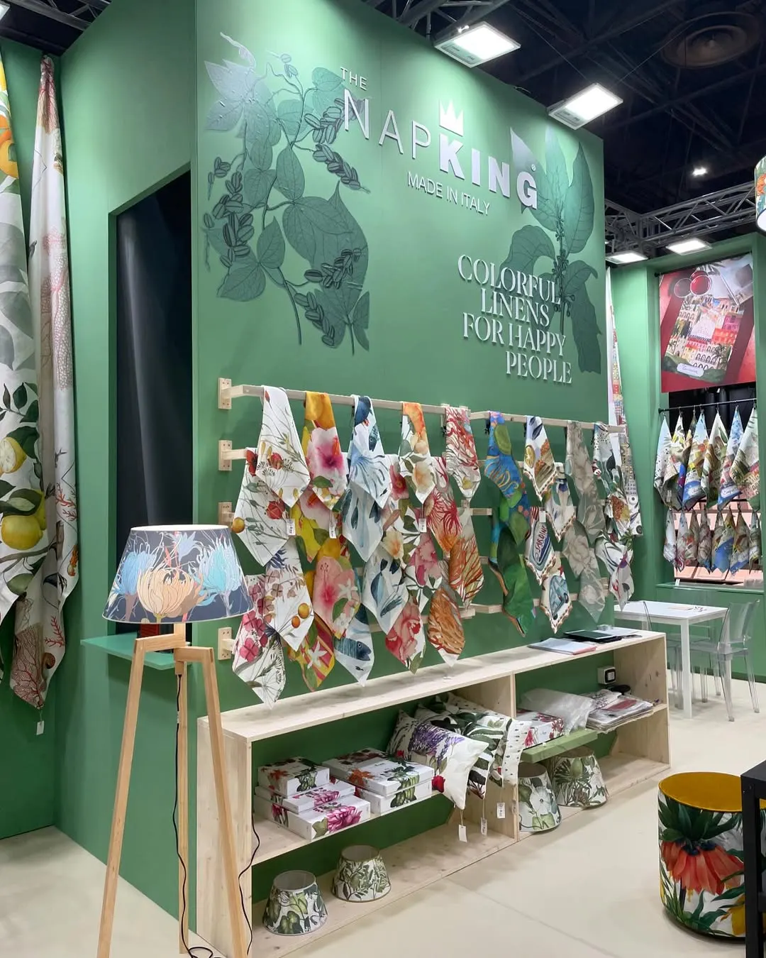 Stand fiera con pareti verdi, tessuti appesi e la scritta Napking
