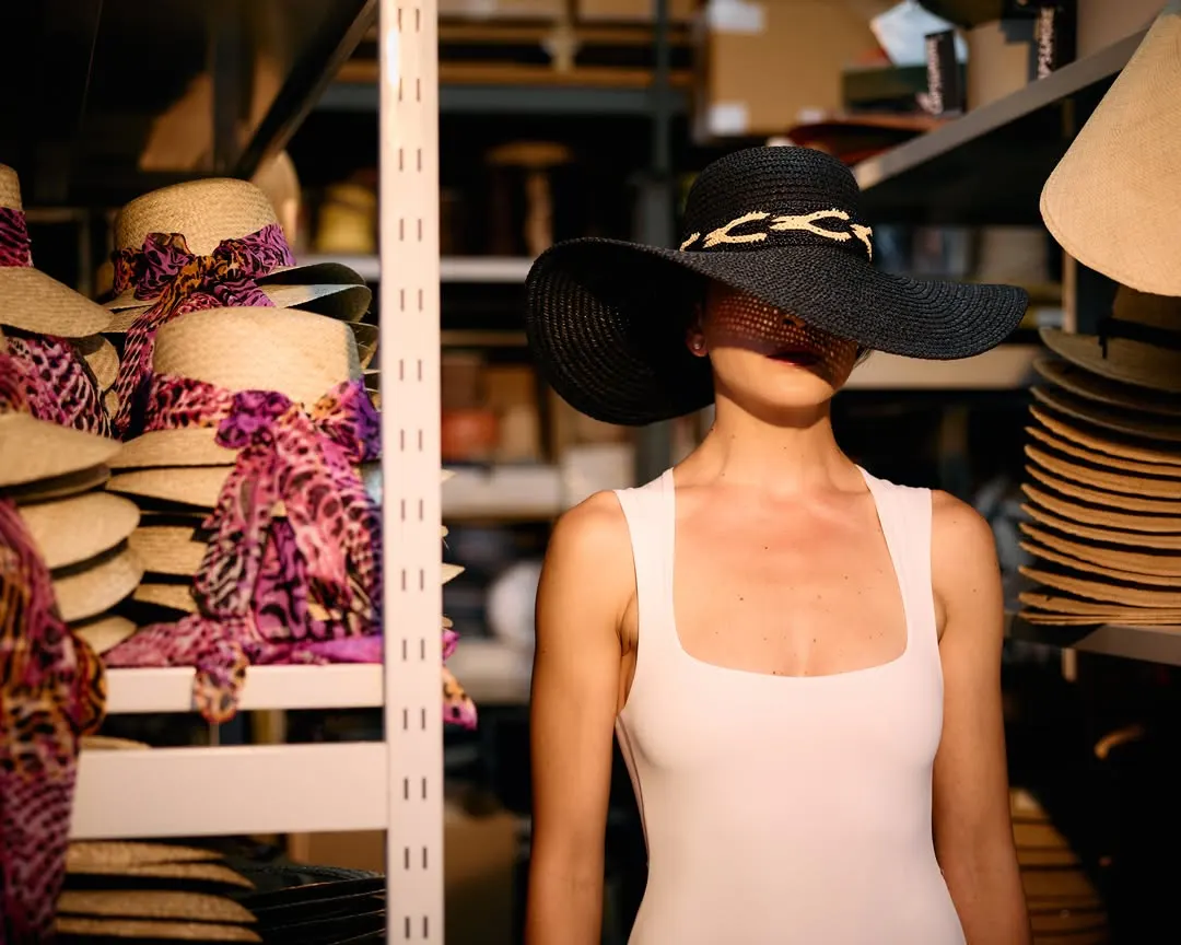 Immagine generata: cappello nero a falda larga fra scaffali di cappelli e nastri colorati