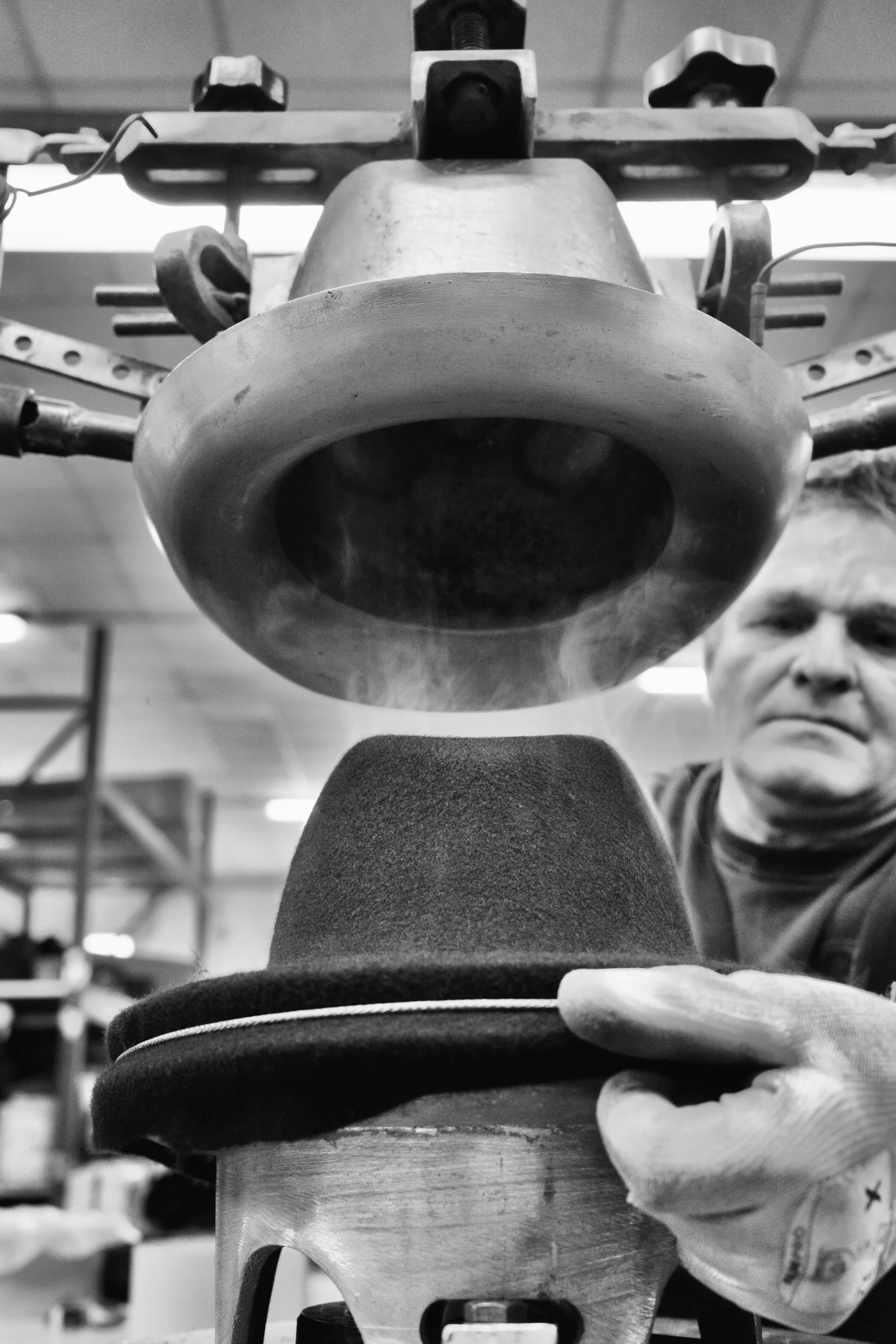 Cappello nero pressato su una forma, le mani dell’operaio sulla macchina