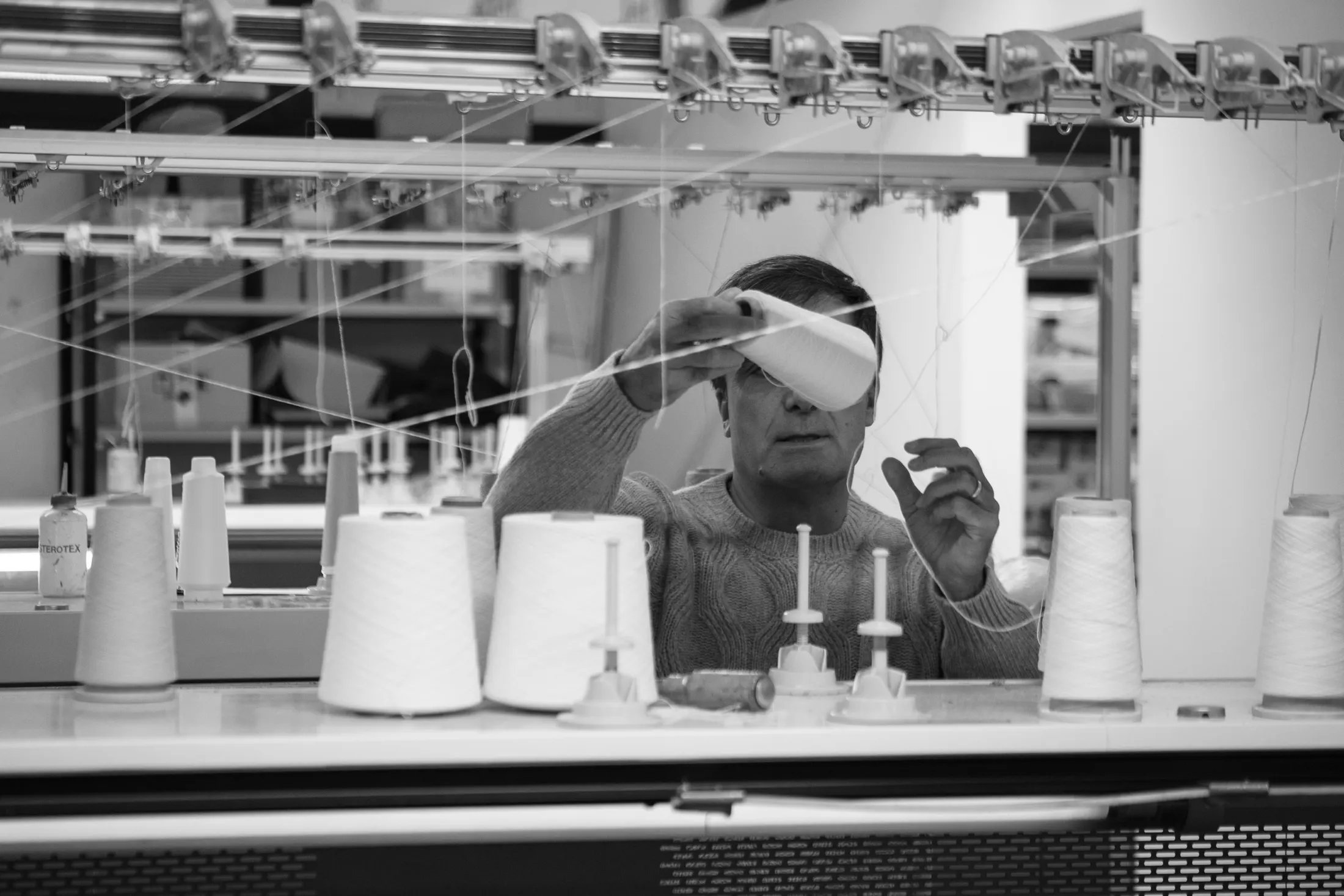 Tecnico al telaio circolare fra i coni di filato, bianco e nero